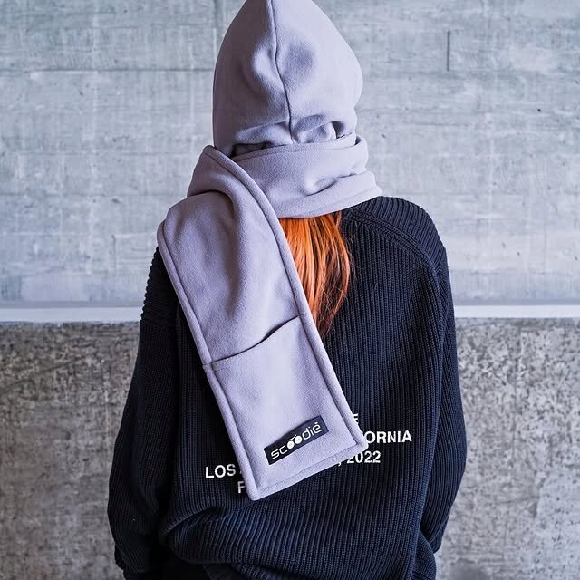 Osoba ubrana w szary kaptur z odpinanym szalikiem, na którym widnieje logo \'scoodie\'. Na czarnym swetrze znajduje się napis \'LOS ANGELES CALIFORNIA EST. 2022\'.