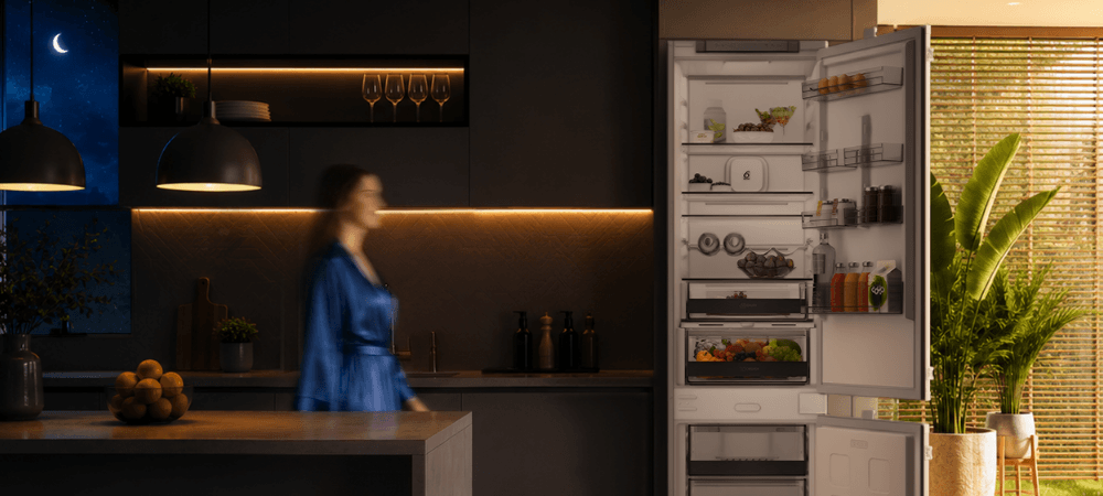 LODÓWKA WHIRLPOOL WHK WHK2 5294 B6E1 Lodówka Whirlpool stoi w kuchennej zabudowie obok dużej rośliny doniczkowej. Po lewej stronie widoczna jest rozmyta sylwetka osoby, a w lewym górnym rogu znajduje się ikona księżyca wykończenie inox elegancki wygląd ponadczasowy design