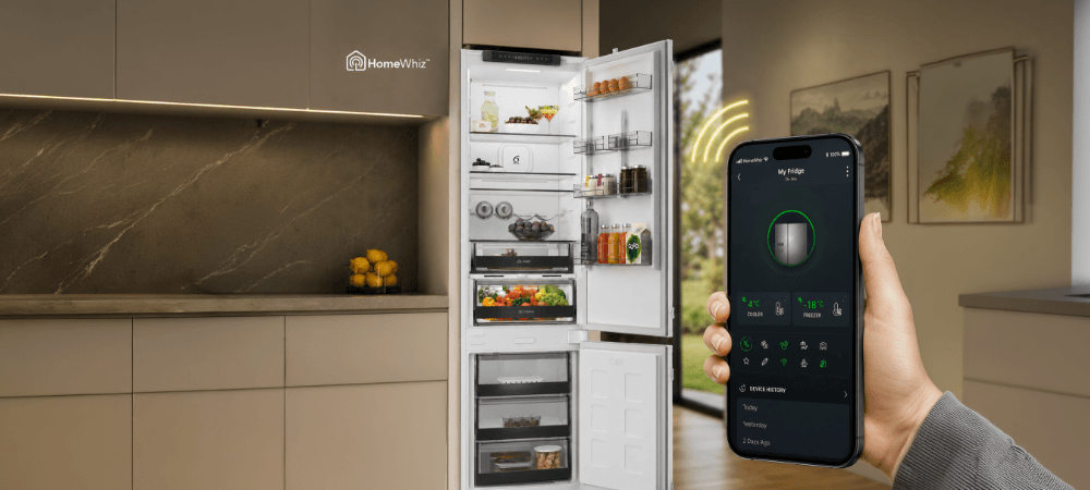LODÓWKA WHIRLPOOL WHK2 5293 B5E Smartfon z ekranem aplikacji HomeWhiz trzymany na pierwszym planie, a w tle widoczna jest lodówka w kuchni. Nad telefonem znajdują się żółte fale symbolizujące połączenie bezprzewodowe HomeWhiz zdalne sterowanie smartfon alert otwartych drzwi