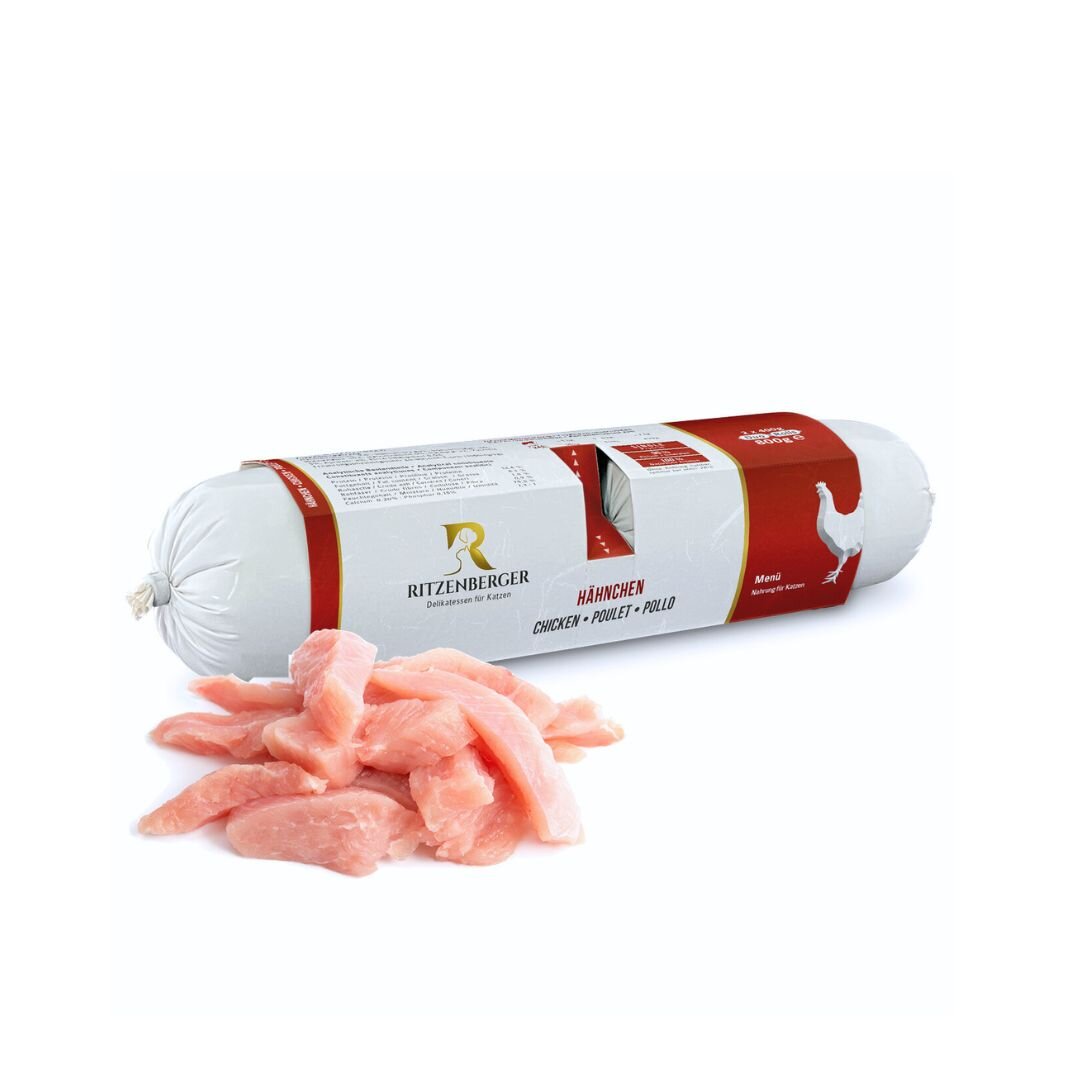 Na obrazie widoczna jest rolka karmy dla kota marki Ritzenberger z etykietą w kolorze czerwonym i białym oraz kawałki surowego mięsa. Na etykiecie znajduje się napis \'Hähnchen Chicken Poulet Pollo\'.