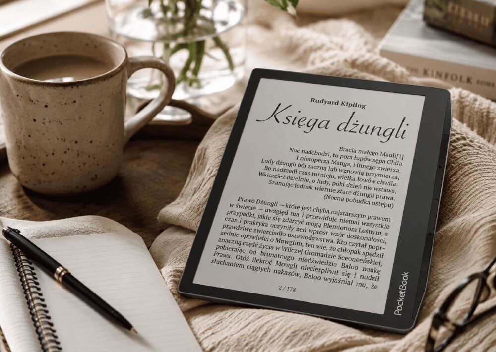 Czytnik e-booków POCKETBOOK Era Lite Czytnik e-booków wyświetlający tekst książki 'Księga dżungli' leży na kocu obok kubka z napojem, notesu z długopisem i okularów, wyświetlacz, rozdzielczość, podświetlenie, obsługa