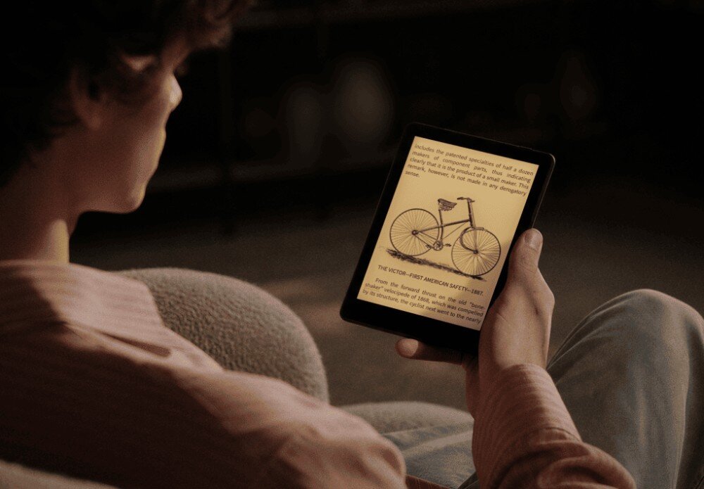 Czytnik e-booków ONYX Boox Go Osoba siedząca tyłem w fotelu trzyma w ręce włączony czytnik z ilustracją roweru na ekranie w ciemnym pomieszczeniu, ekran, rozdzielczość, podświetlenie