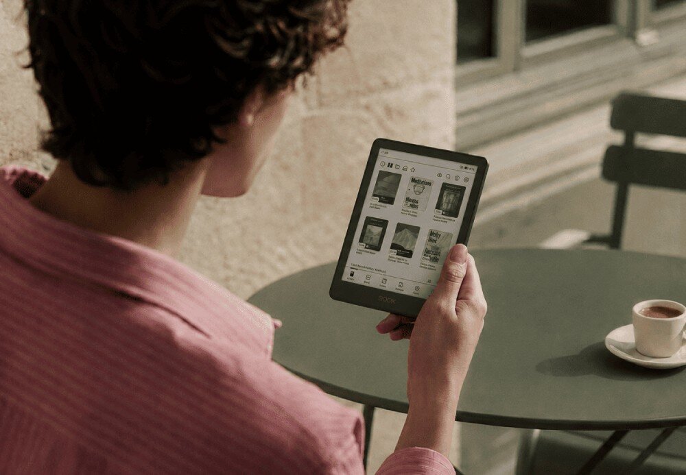 Czytnik e-booków ONYX Boox Go Mężczyzna w różowej koszuli trzyma włączony czytnik w dłoniach, siedząc przy okrągłym stoliku w kawiarni na zewnątrz, pamięć, czytnik kart microSD, formaty