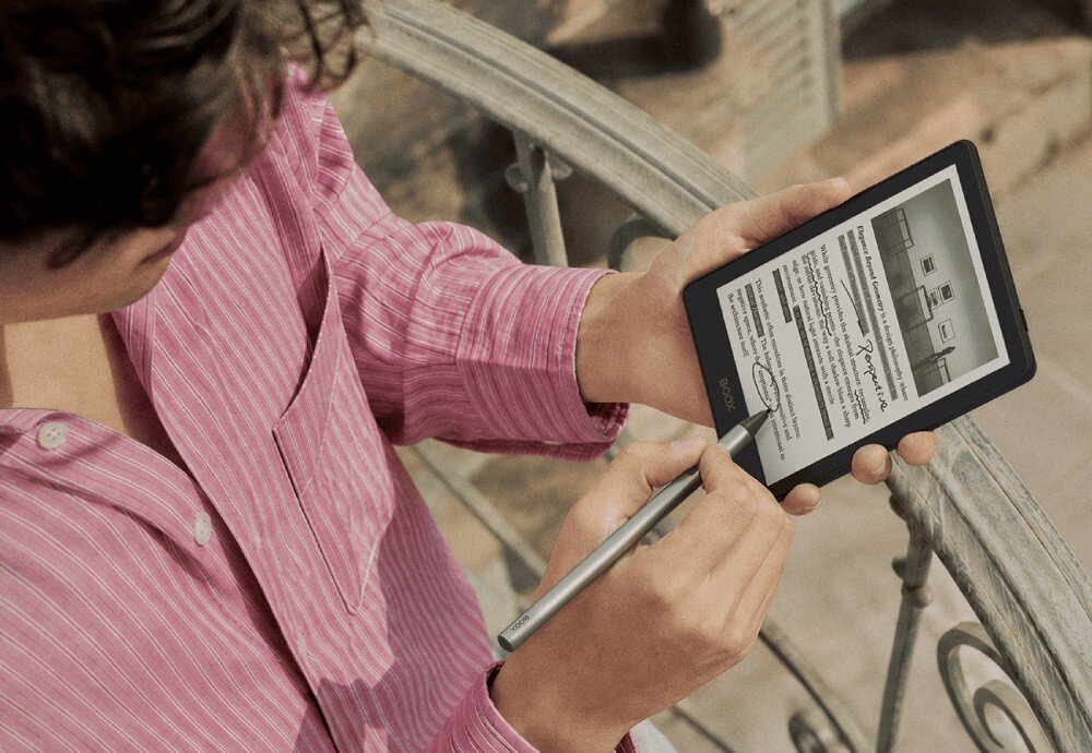 Czytnik e-booków ONYX Boox Go Mężczyzna w paski koszuli trzyma czytnik i pisze rysikiem po ekranie, stojąc na balkonie z ozdobną barierką, akumulator, złącze USB-C