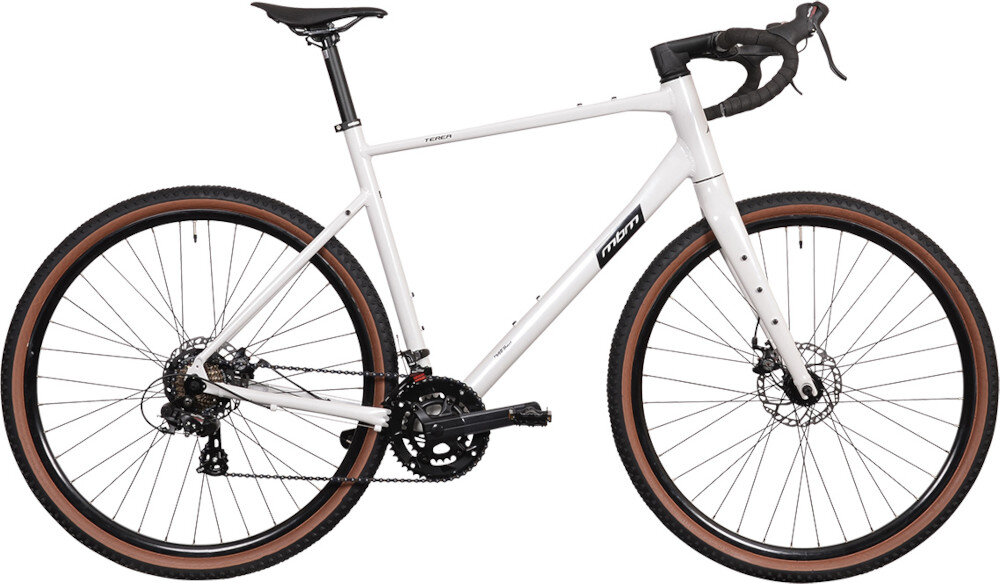Biały rower gravel z czarnymi elementami, takimi jak siodełko i kierownica, oraz brązowymi oponami. Na ramie widoczne jest logo \'MBM\'.