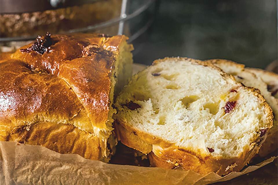 W prosty sposób rozmrażaj pieczywo dzięki wykorzystaniu funkcji Bread Defrost Na obrazie widoczny jest świeżo upieczony chleb z chrupiącą, złocistą skórką i kawałkami suszonych owoców w środku. Chleb jest częściowo pokrojony na kromki, leżące na papierze do pieczenia.