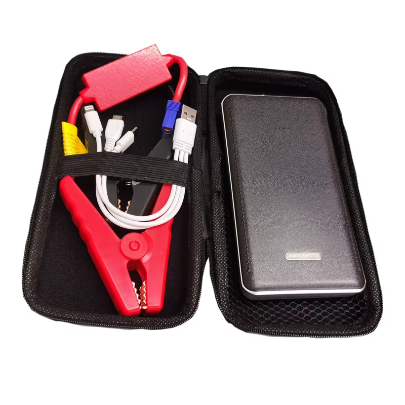Na zdjęciu znajduje się otwarte etui zawierające urządzenie rozruchowe z kablami i powerbankiem. Widoczne są czerwone kable z zaciskami oraz czarny powerbank z napisem \'JUMPSTARTER\'.