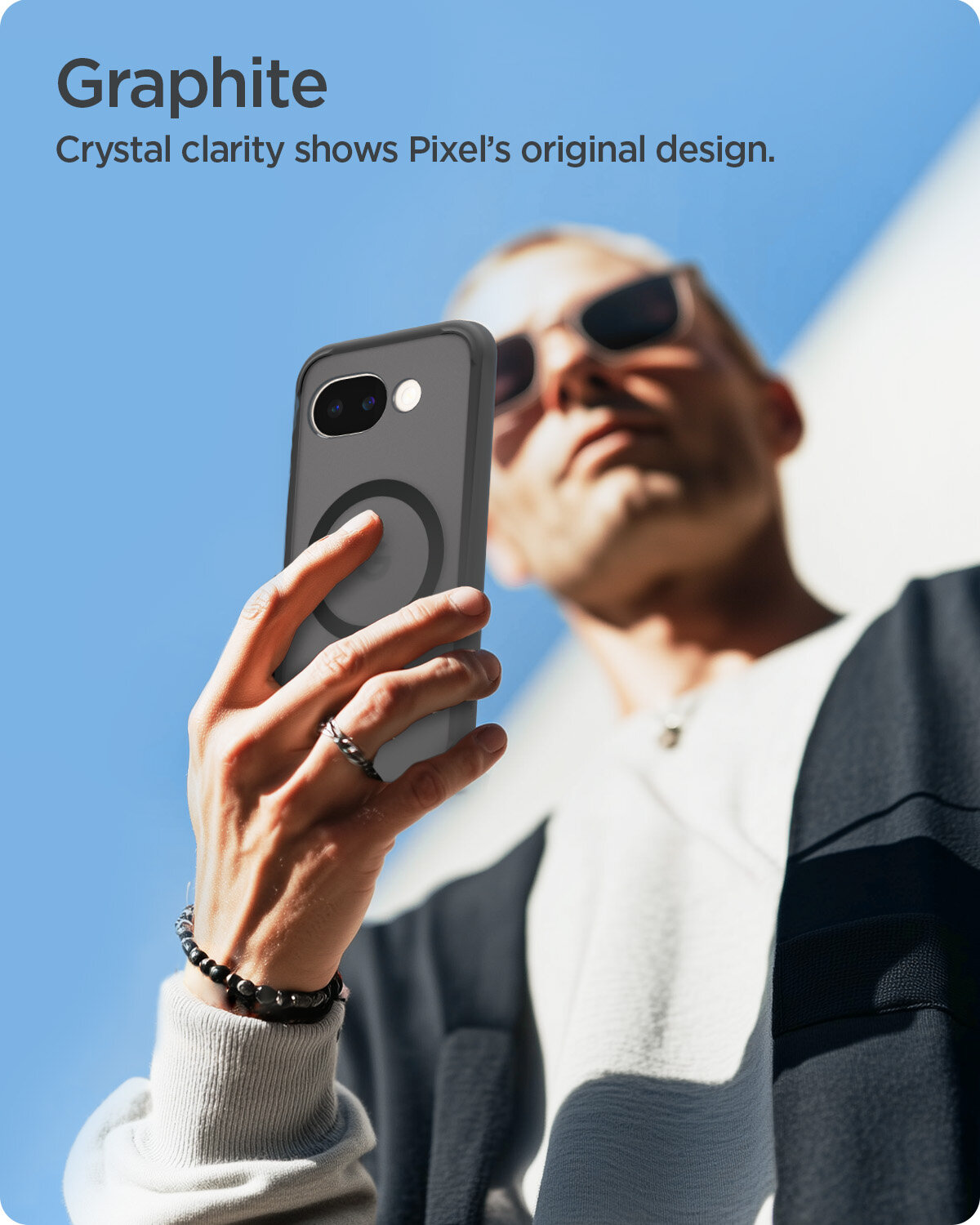 Osoba trzyma telefon w etui z widocznym okrągłym wzorem, na tle nieba. Tekst na obrazie: \'Graphite Crystal clarity shows Pixel’s original design.\'
