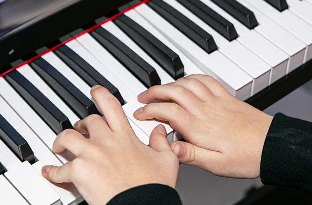 Dwie dłonie grają na klawiaturze pianina cyfrowego, widoczne są czarno-białe klawisze.