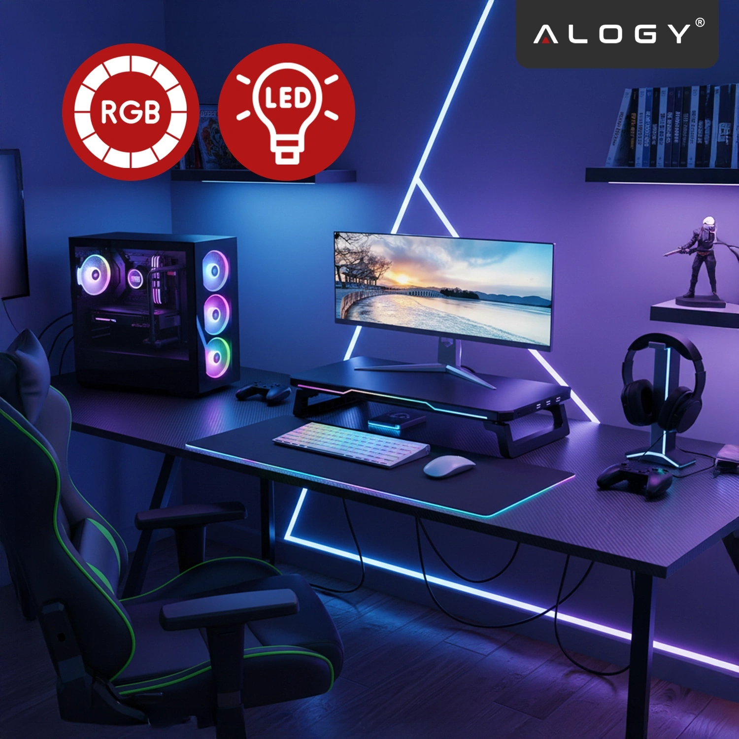 Na biurku znajduje się monitor na czarnej podstawce z oświetleniem RGB, obok klawiatura i mysz. W tle widoczny jest komputer z podświetleniem RGB oraz logo \'ALOGY\'.