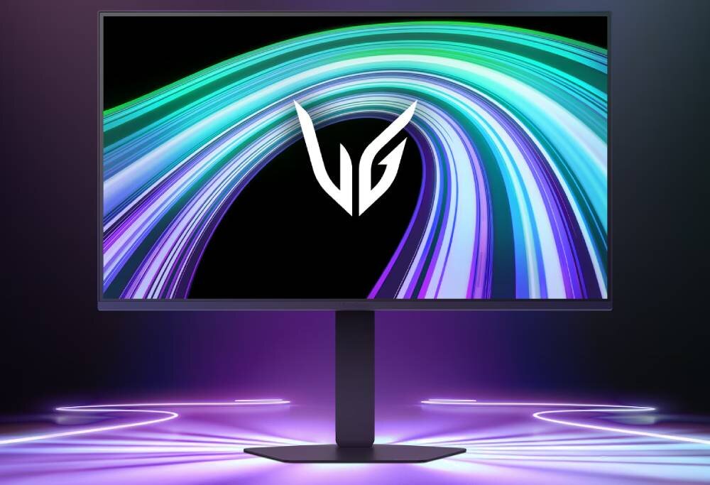 Monitor z wyświetlaczem pokazującym kolorowe, zakrzywione linie na czarnym tle oraz logo \'VG\'. Podstawa monitora jest prosta, a tło jest oświetlone fioletowym światłem.