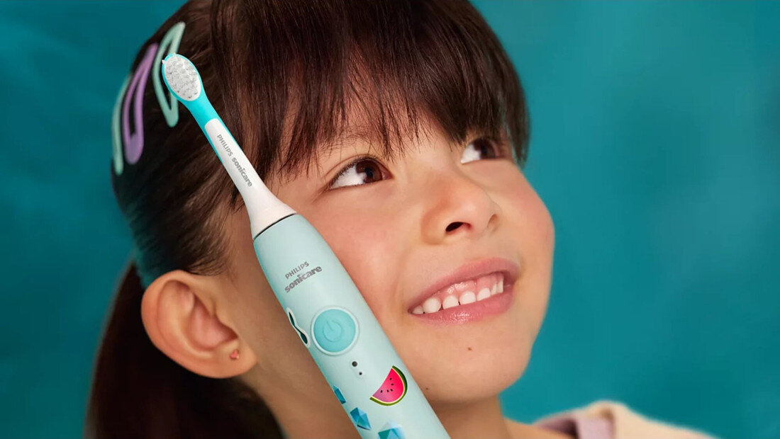 Dziecko trzyma turkusową szczoteczkę soniczną z kolorowymi wzorami, na której widnieje napis \'PHILIPS Sonicare\'.