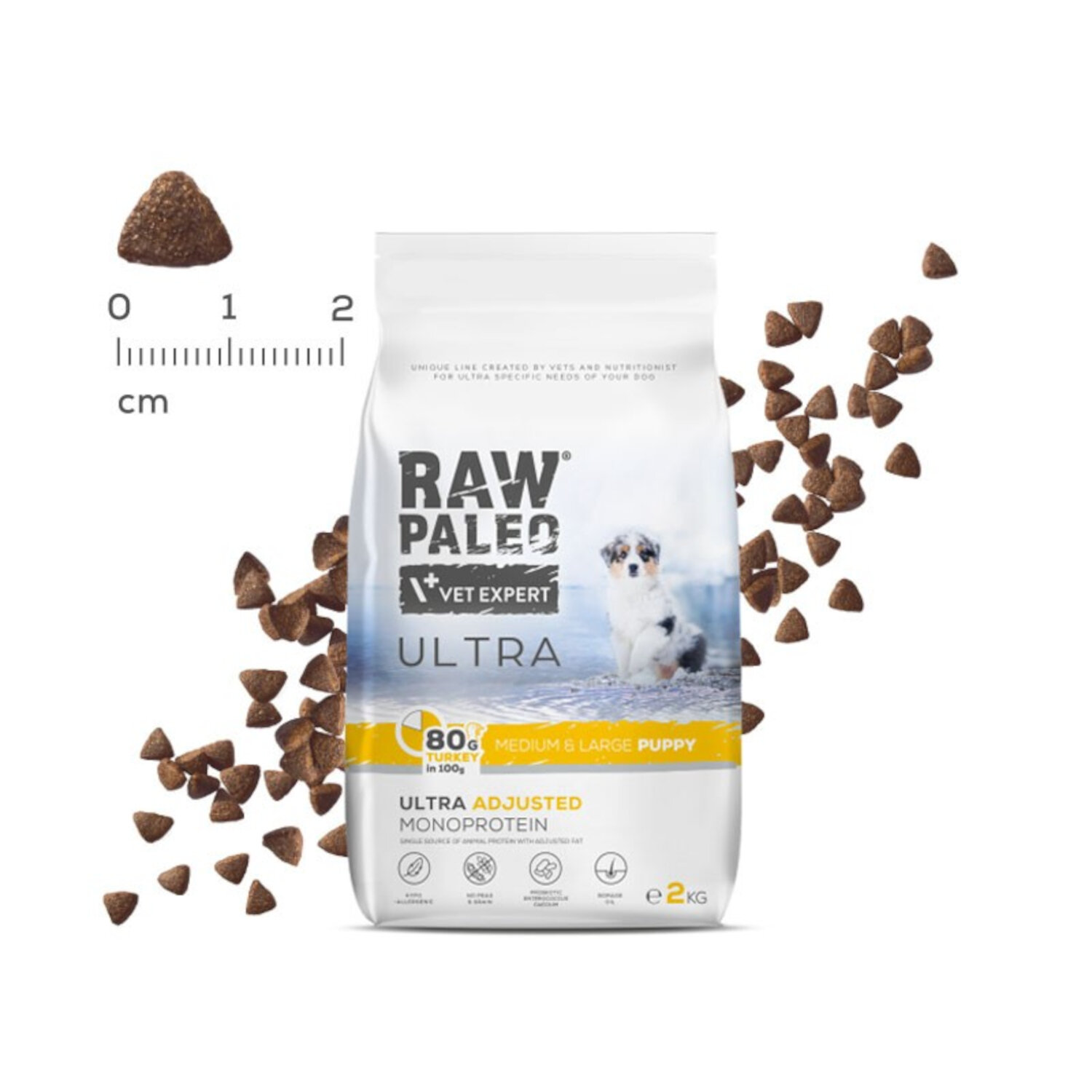 Opakowanie suchej karmy dla szczeniąt z napisem \'RAW PALEO VET EXPERT ULTRA\'. Obok widoczne są granulki karmy oraz miarka w centymetrach.