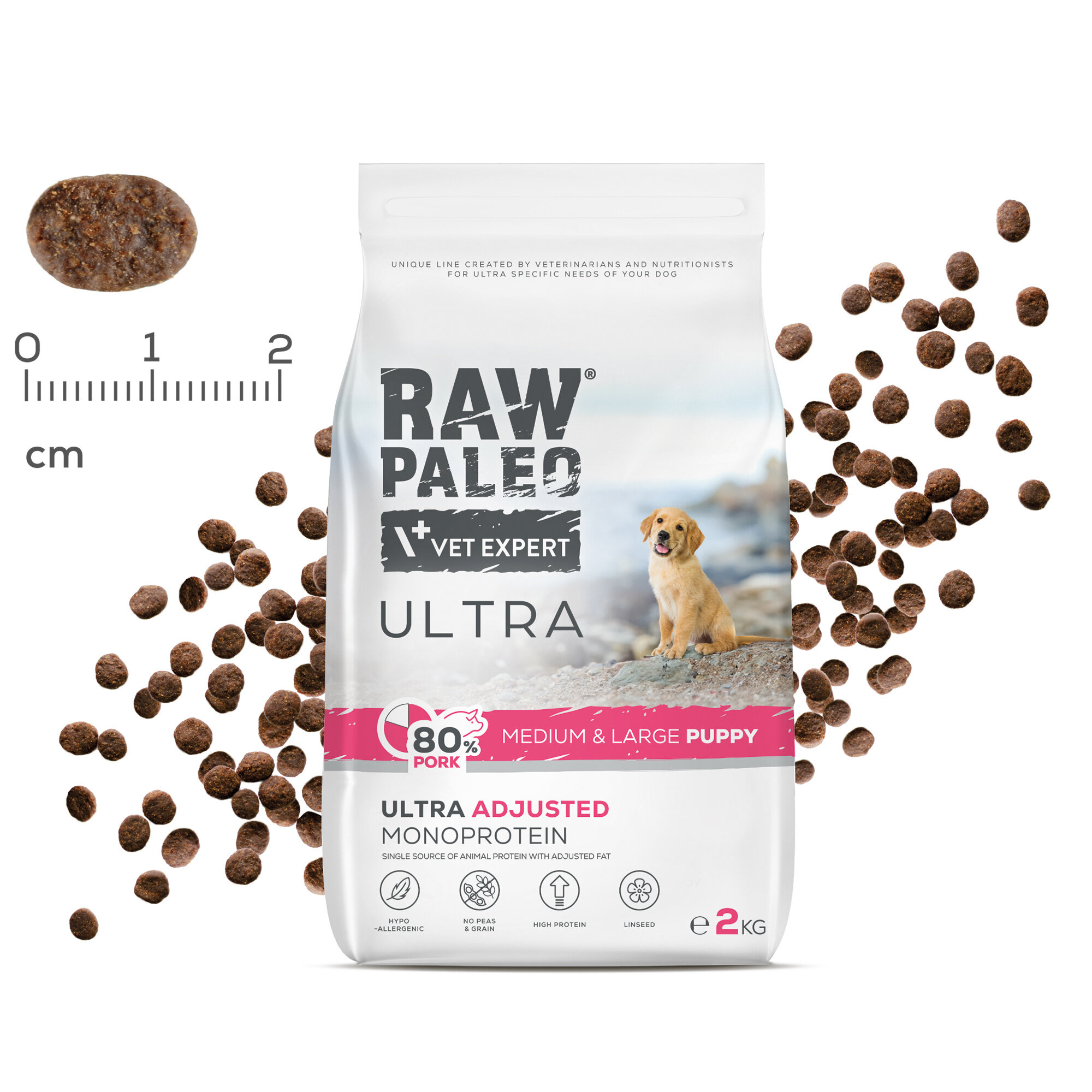 Opakowanie suchej karmy dla szczeniąt z napisem \'RAW PALEO VET EXPERT ULTRA\' oraz \'80% PORK MEDIUM & LARGE PUPPY\'. Obok opakowania widoczne są granulki karmy i miarka w centymetrach.