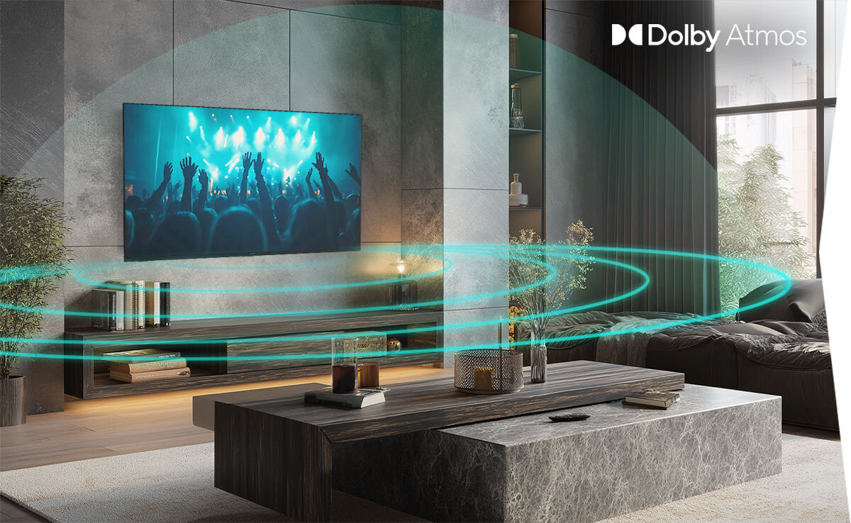 W nowoczesnym salonie na ścianie wisi telewizor wyświetlający koncert, a w prawym górnym rogu widoczne jest logo \'Dolby Atmos\'.