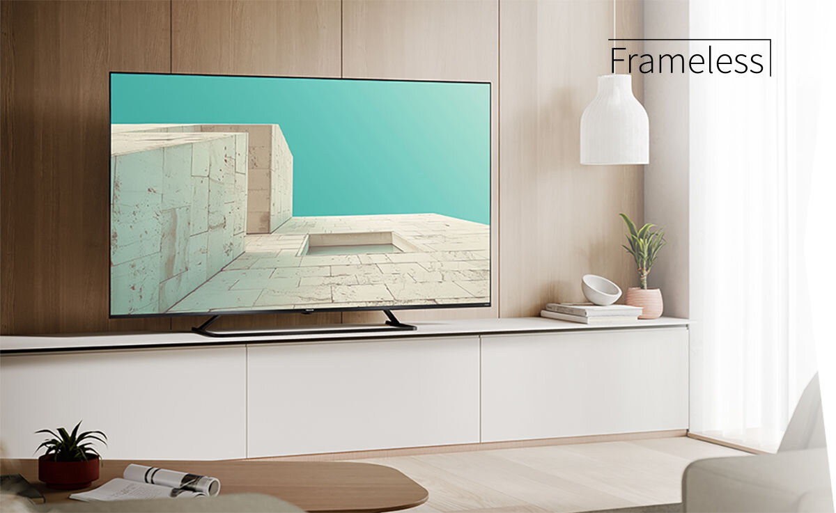 Telewizor z cienką ramką wyświetla obraz przedstawiający architekturę z jasnymi ścianami i niebieskim niebem. Obok telewizora znajduje się napis \'Frameless\'.