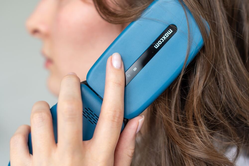 Osoba trzyma przy uchu niebieski telefon z widocznym logo \'MAXCOM\'.