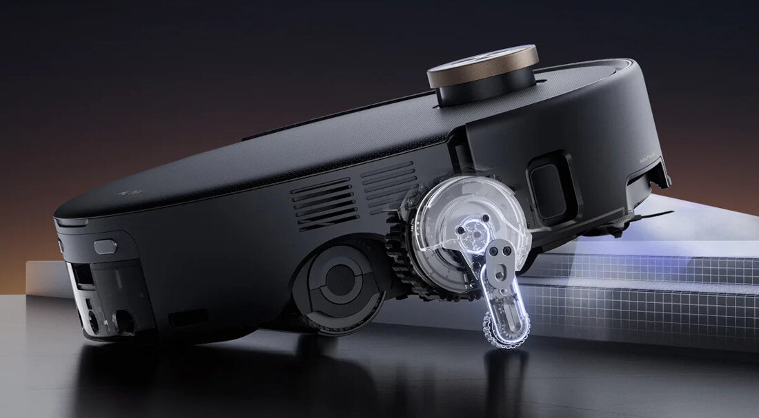 Czarny robot sprzątający z widocznym mechanizmem kół i czujnikiem na górze. Urządzenie jest ustawione pod kątem, ukazując szczegóły konstrukcji.