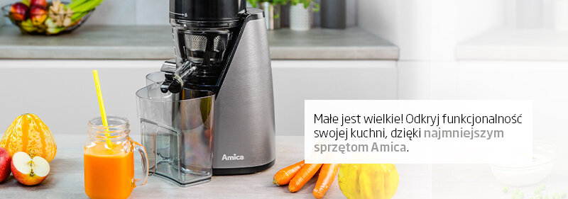 Na blacie kuchennym stoi urządzenie marki Amica obok szklanki z pomarańczowym napojem i warzyw. Widoczny tekst: \'Małe jest wielkie! Odkryj funkcjonalność swojej kuchni, dzięki najmniejszym sprzętom Amica.\'