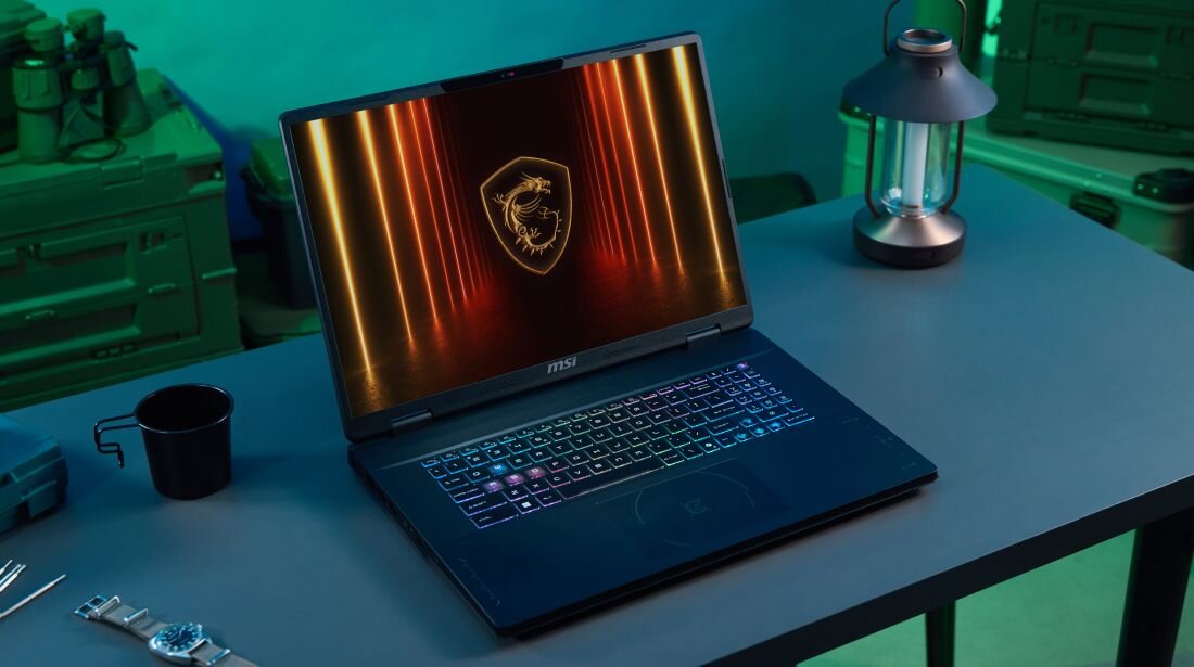 Laptop MSI Crosshair z podświetlaną klawiaturą RGB stoi na biurku, prezentując smukłą konstrukcję do mobilnego gamingu – gabaryty 3,1 kg i grubość do 30 mm