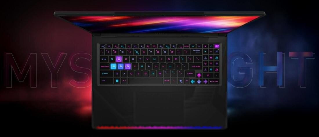 Laptop z podświetlaną klawiaturą w różnych kolorach, widoczny z góry. W tle rozmyty napis \'MYSTIC LIGHT\'.