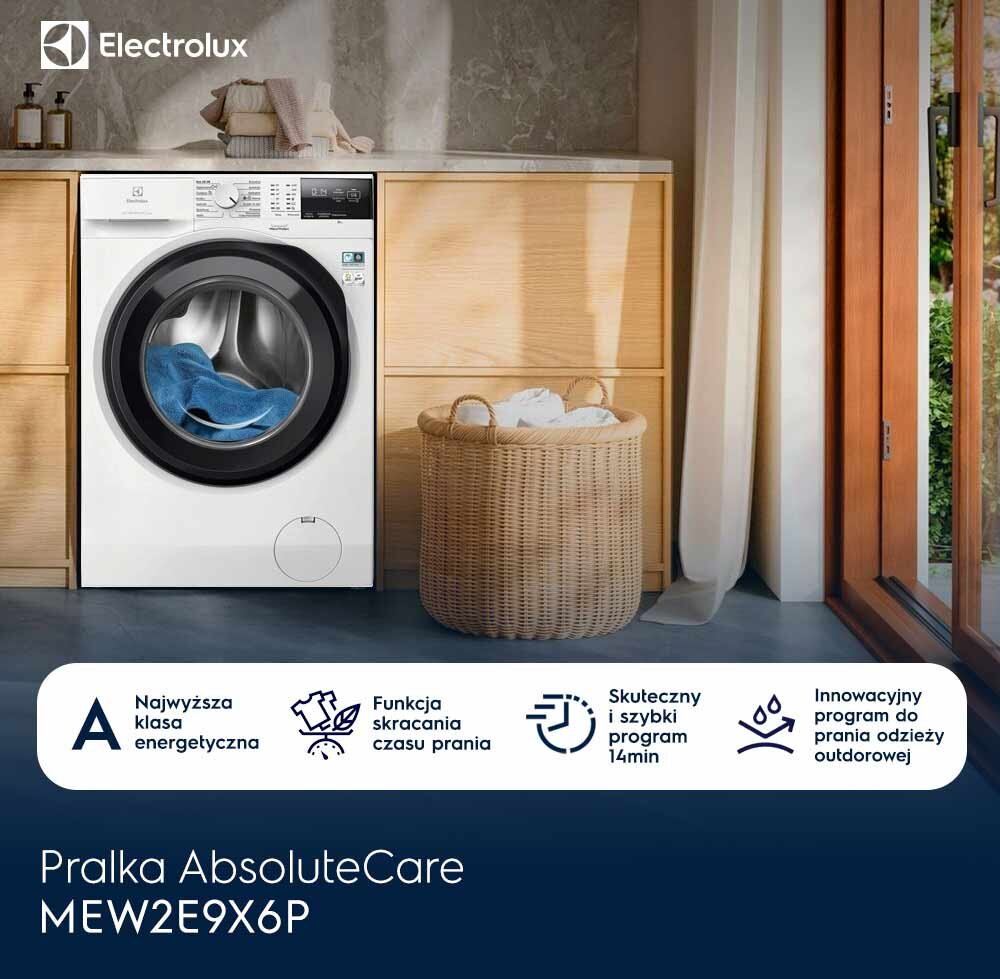 Na obrazie znajduje się pralka z logo Electrolux, umieszczona w drewnianej zabudowie. Obok pralki stoi kosz z praniem, a na dole widnieje napis: \'Pralka AbsoluteCare MEW2E9X6P\'.