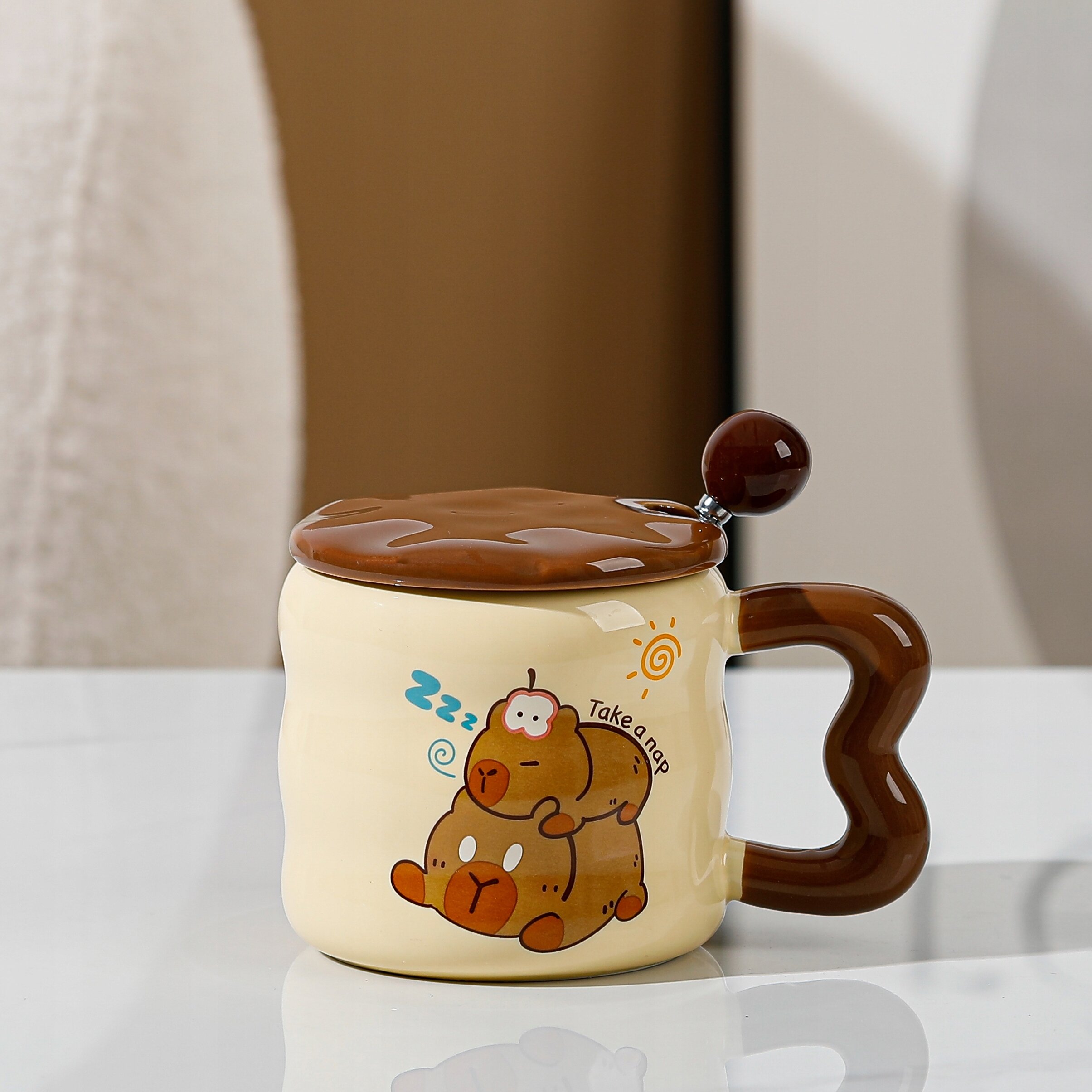Ceramiczny kubek z brązowym uchwytem i pokrywką, ozdobiony rysunkiem dwóch śpiących misiów oraz napisem \'Take a nap\'.