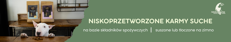 Pies stoi przy stole, na którym znajdują się dwie torby karmy. Tekst na zielonym tle: \'NISKOPRZETWORZONE KARMY SUCHE na bazie składników spożywczych | suszone lub tłoczone na zimno\'.