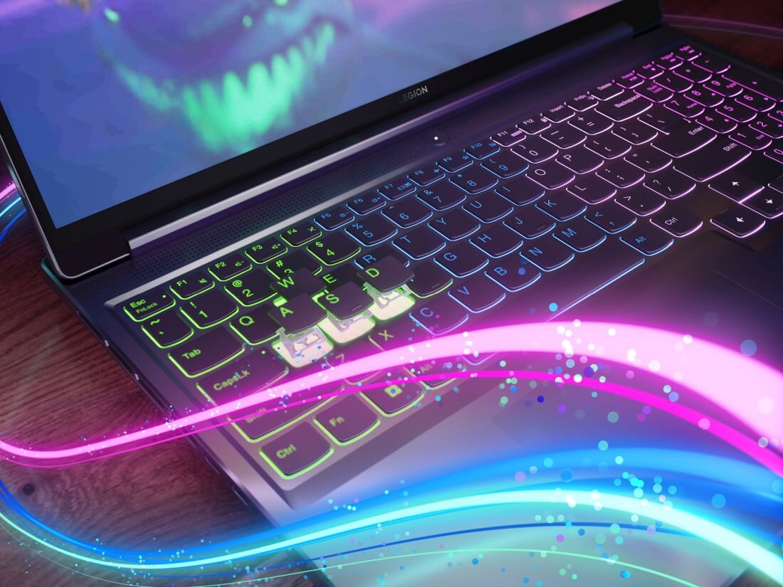Laptop z podświetlaną klawiaturą, na której widoczne są różnokolorowe efekty świetlne. Na ekranie wyświetlany jest obraz z zielonymi elementami, a na obudowie znajduje się logo \'LEGION\'.
