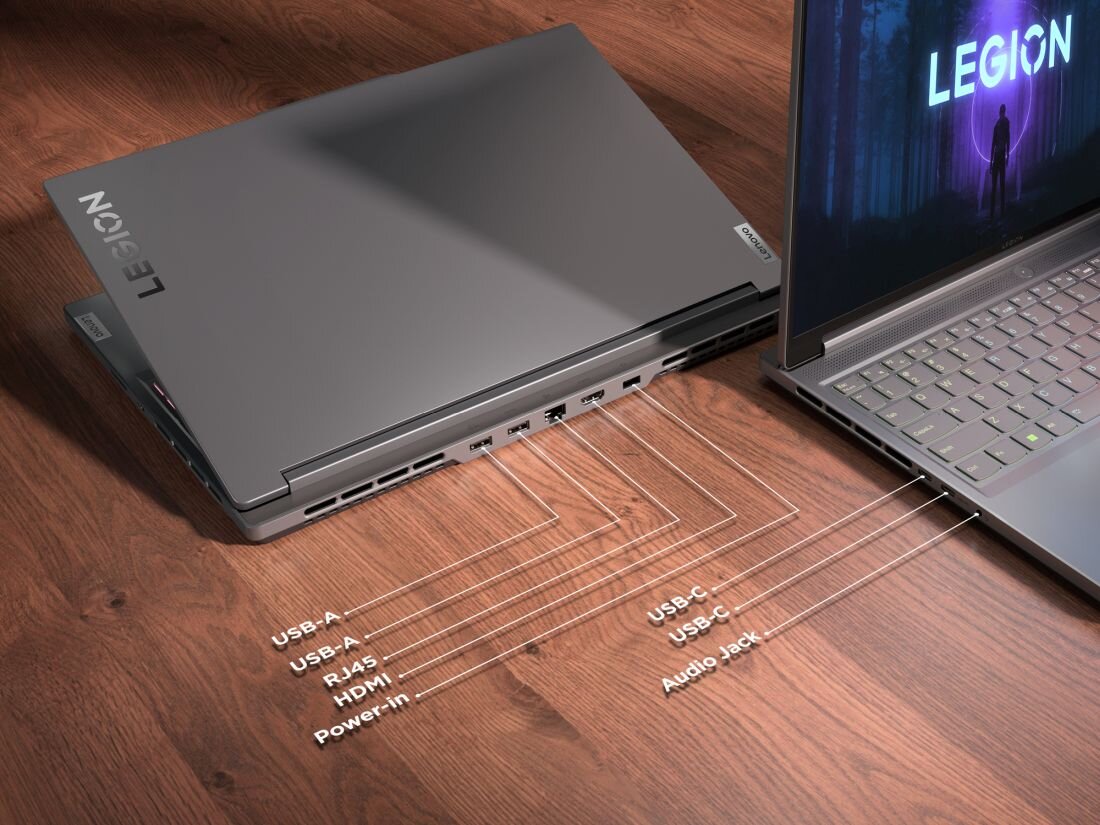 Na drewnianym blacie znajdują się dwa laptopy z widocznymi portami: USB-A, USB-C, RJ45, HDMI, Power-in oraz Audio Jack. Na ekranie jednego z laptopów widnieje napis \'LEGION\'.