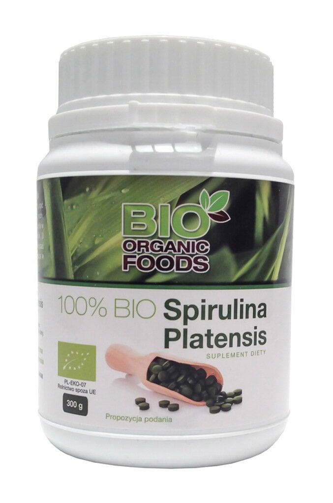 Biały pojemnik z etykietą przedstawiającą zielone liście i napis \'BIO ORGANIC FOODS\'. Na etykiecie widnieje tekst \'100% BIO Spirulina Platensis SUPLEMENT DIETY\', a poniżej znajduje się obrazek z zielonymi tabletkami i napis \'Propozycja podania\'.