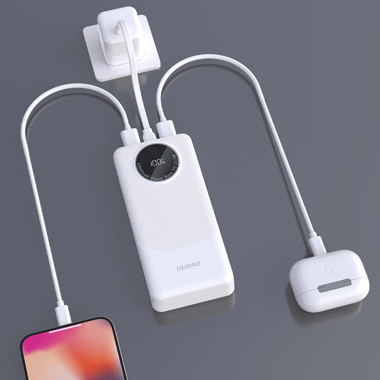 Na obrazie widoczny jest biały powerbank z wyświetlaczem pokazującym \'100%\' oraz napisem \'20000mAh Power Bank 22.5W\'. Powerbank jest podłączony do dwóch urządzeń za pomocą kabli USB, a na jego obudowie znajduje się logo \'DUDAO\'.