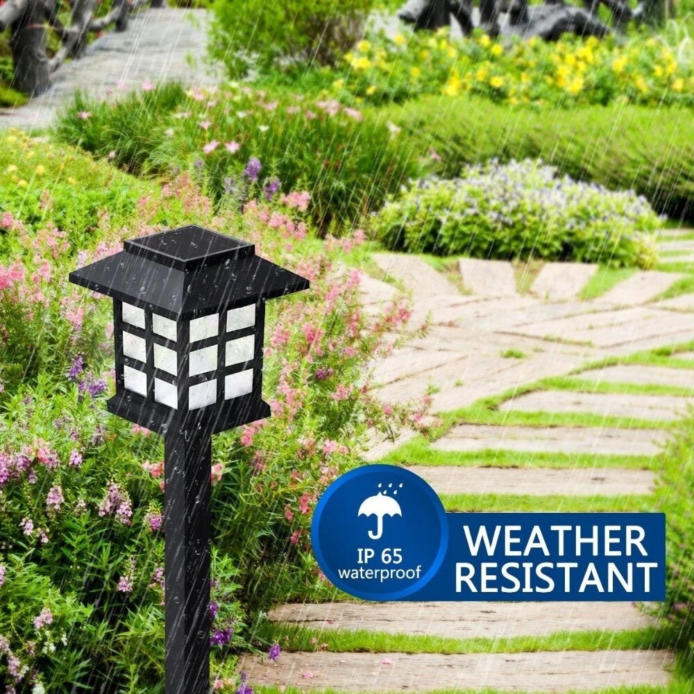 Na obrazie widać czarną lampę solarną w kształcie słupka, umieszczoną w ogrodzie podczas deszczu. Obok lampy znajduje się napis \'IP 65 waterproof WEATHER RESISTANT\'.