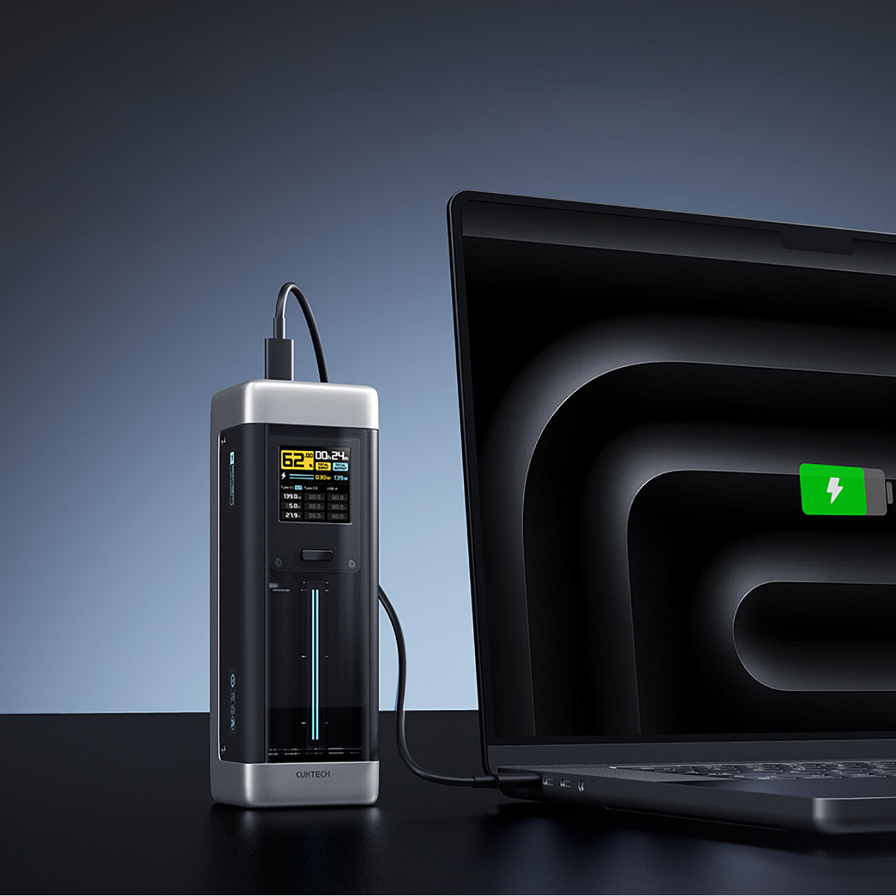 Na obrazie widać czarny powerbank z wyświetlaczem, podłączony do laptopa, na którym widoczna jest ikona ładowania baterii. Na wyświetlaczu powerbanka znajdują się różne informacje, w tym liczba \'62\'.