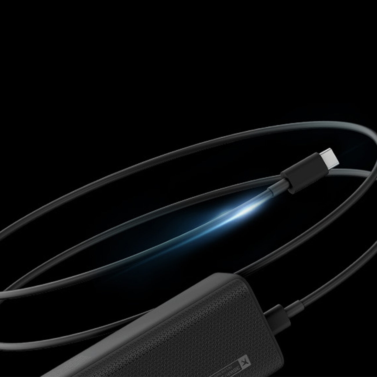 Na czarnym tle widoczny jest czarny powerbank z podłączonym kablem USB-C, wokół którego biegnie świetlisty efekt. Powierzchnia powerbanka ma teksturowane wykończenie.