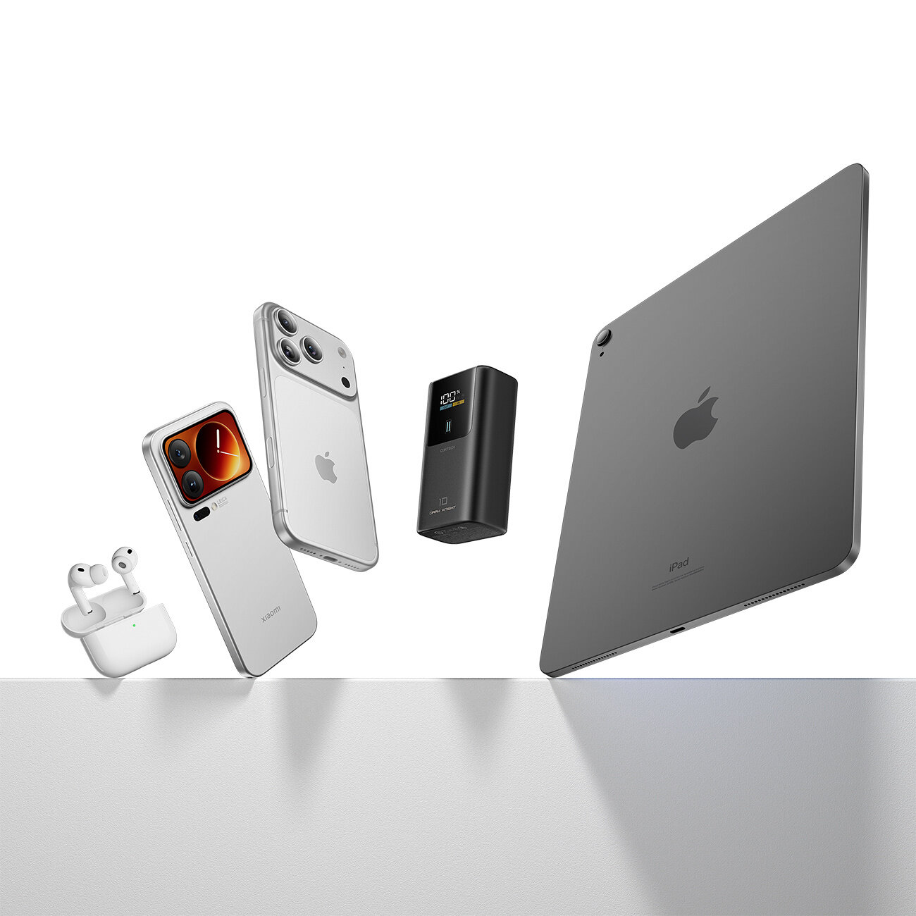 Na obrazie widoczne są różne urządzenia elektroniczne, w tym smartfon, tablet, słuchawki bezprzewodowe i powerbank. Powerbank ma wyświetlacz z informacją \'100%\' i jest koloru szarego.