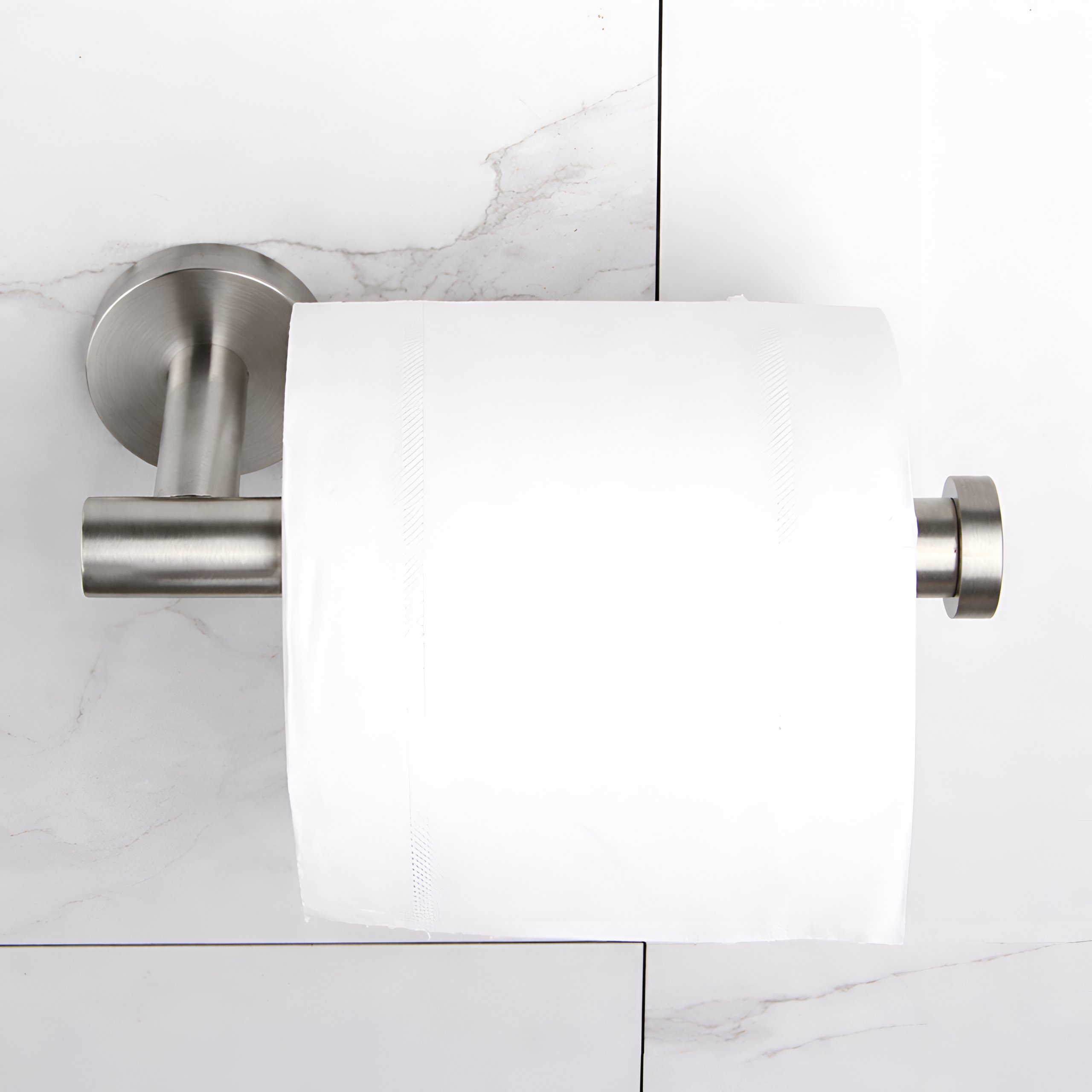Na obrazie widoczny jest metalowy uchwyt na papier toaletowy w kolorze srebrnym, zamontowany na ścianie z białymi płytkami. Na uchwycie znajduje się rolka białego papieru toaletowego.