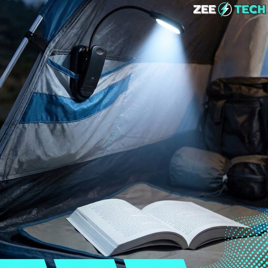 Lampka do czytania z klipsem oświetla otwartą książkę w namiocie. W prawym górnym rogu widoczne jest logo \'ZEE TECH\'.