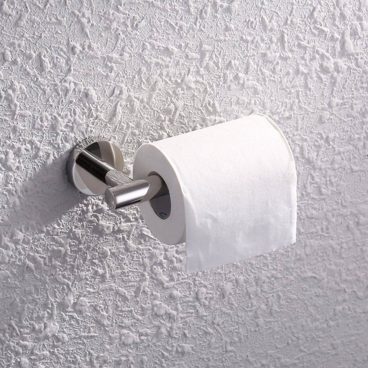 Metalowy uchwyt na papier toaletowy w kolorze chromu zamontowany na ścianie z rolką papieru toaletowego. Ściana ma teksturę przypominającą tynk dekoracyjny.