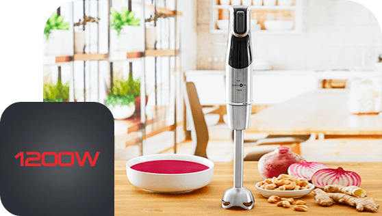 Na drewnianym blacie kuchennym stoi blender ręczny obok miski z czerwonym płynem oraz składników takich jak orzechy i cebula. W rogu obrazu widnieje napis \'1200W\' na ciemnym tle.