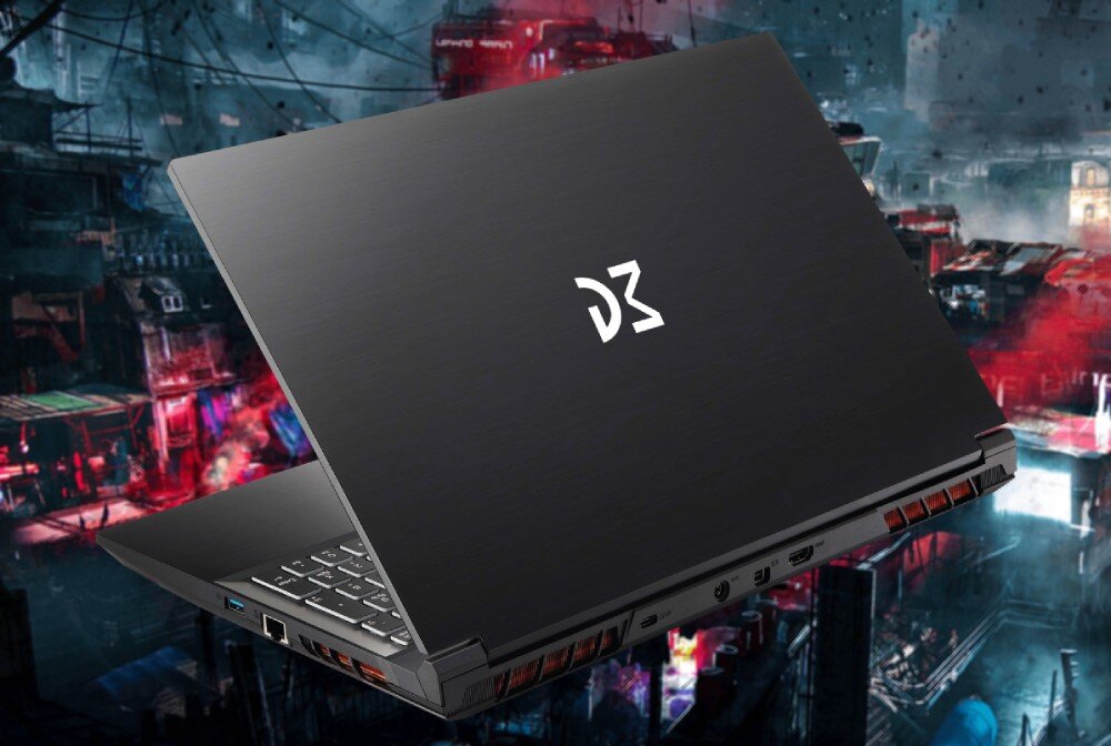 Na obrazie widoczny jest czarny laptop z logo \'D3\' na pokrywie. W tle znajduje się rozmyty, kolorowy krajobraz miejski.