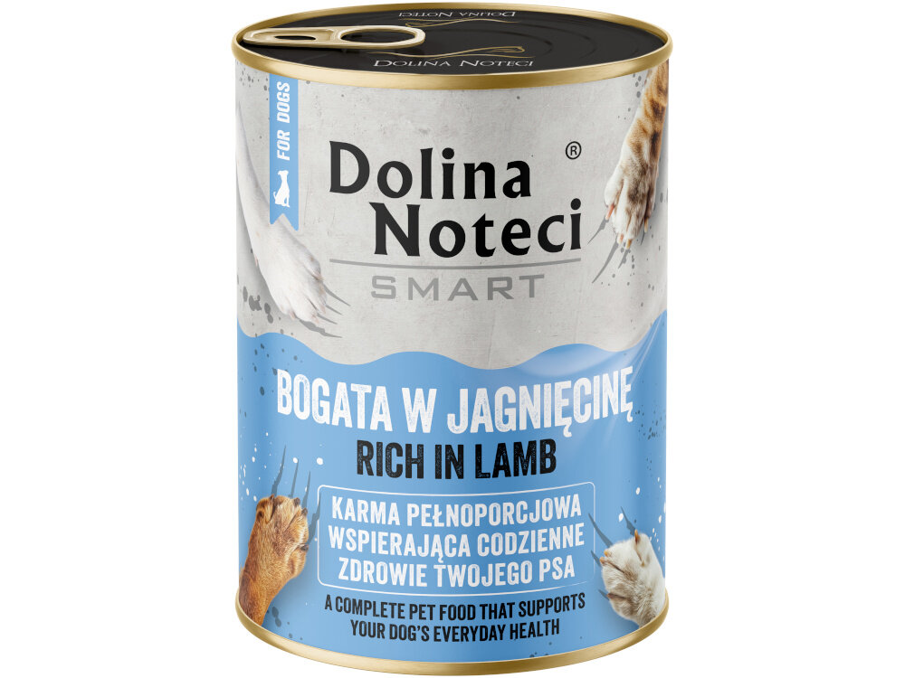Na podłodze kuchni stoją trzy puszki z napisem \'Dolina Noteci SMART BOGATA W JAGNIĘCINĘ RICH IN LAMB\'. W tle znajduje się pies oraz drewniane szafki kuchenne z piekarnikiem.