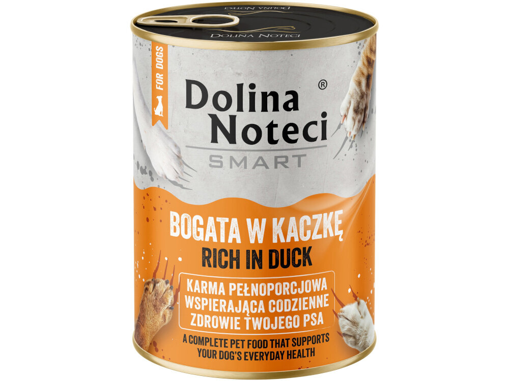 Na podłodze stoi pięć puszek karmy dla psa marki Dolina Noteci Smart, bogatej w kaczkę. Obok puszek widoczne są łapy psa oraz miska i zabawka w tle.