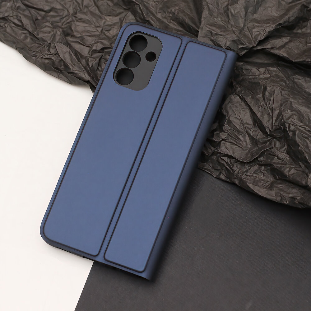 Granatowe etui na telefon z trzema wycięciami na aparaty, leży na ciemnym tle z teksturą przypominającą zmięty papier.