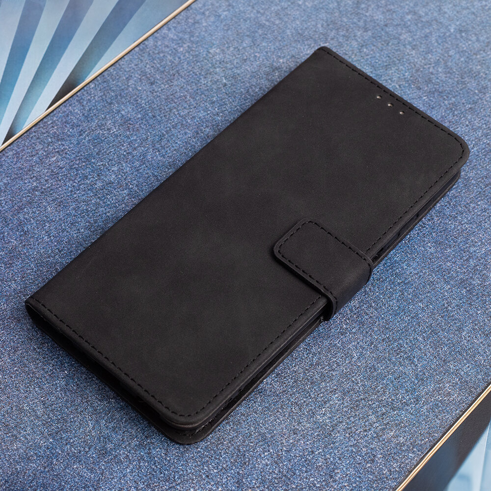 Czarne etui na telefon leży na niebieskiej powierzchni. Etui ma zapięcie na magnes i gładką teksturę.