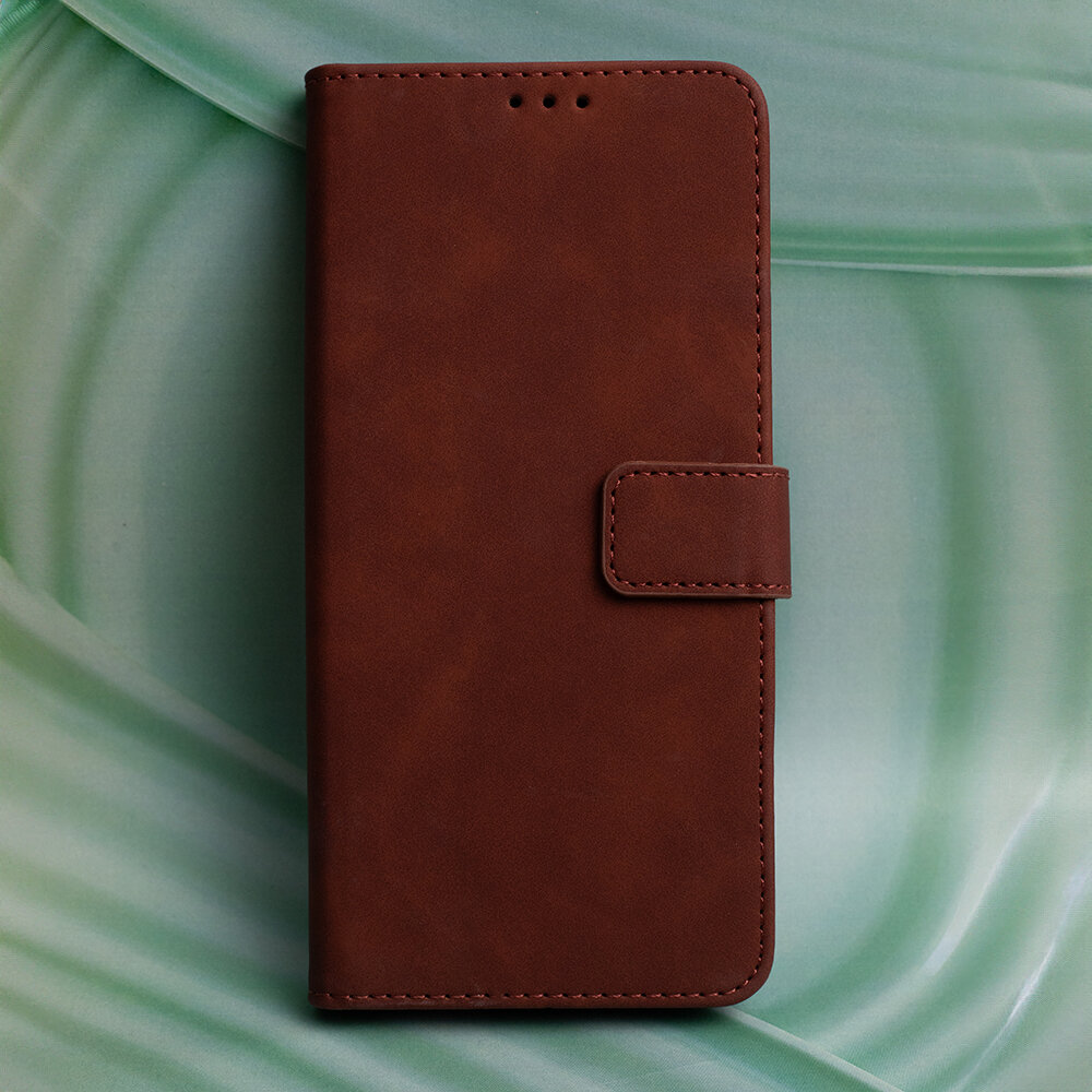 Brązowe etui na telefon z klapką, wykonane z materiału przypominającego skórę, na tle zielonego wzoru. Etui posiada zapięcie na magnes i otwory na głośnik.
