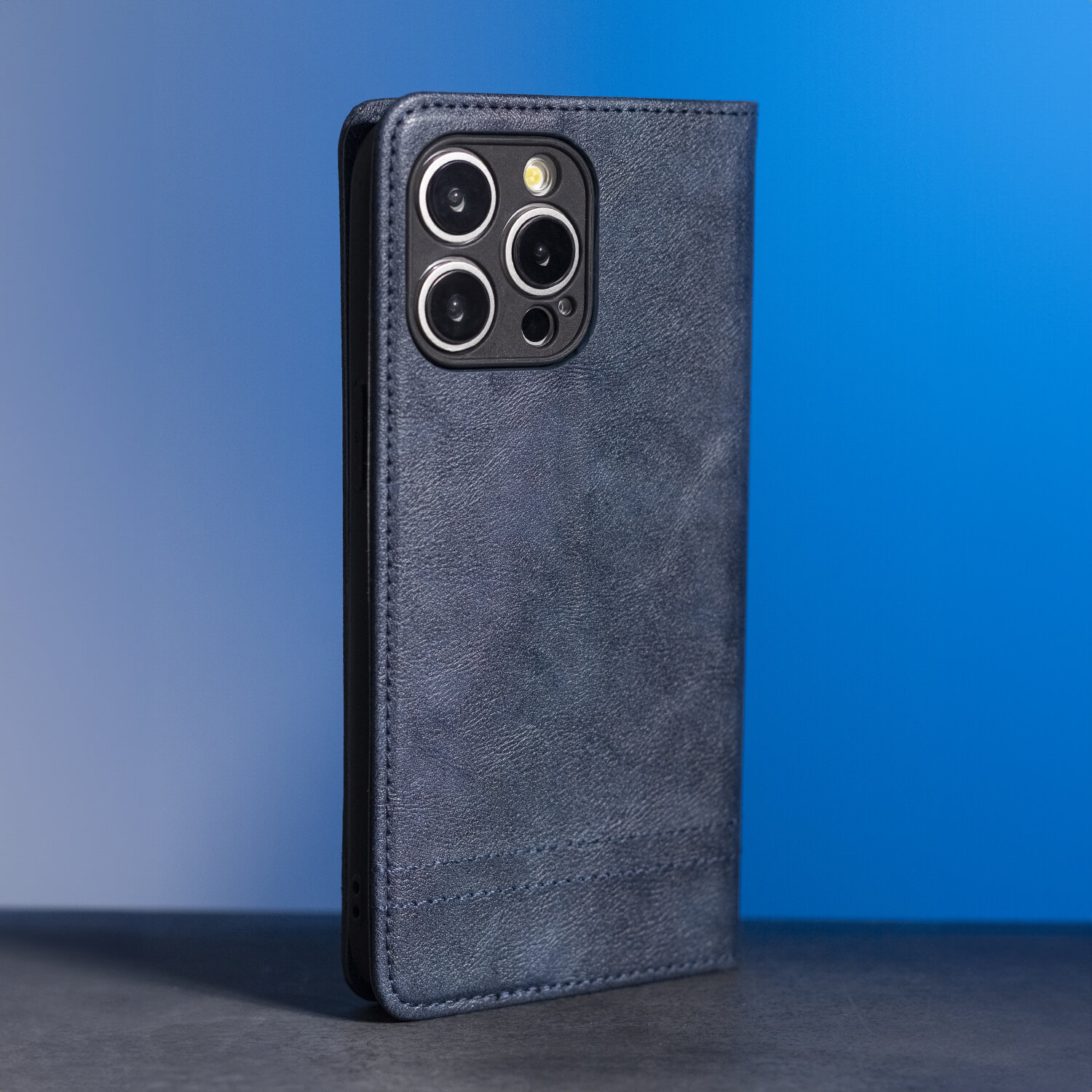 Granatowe etui na telefon z widocznymi wycięciami na aparat fotograficzny. Etui ma teksturę przypominającą skórę.