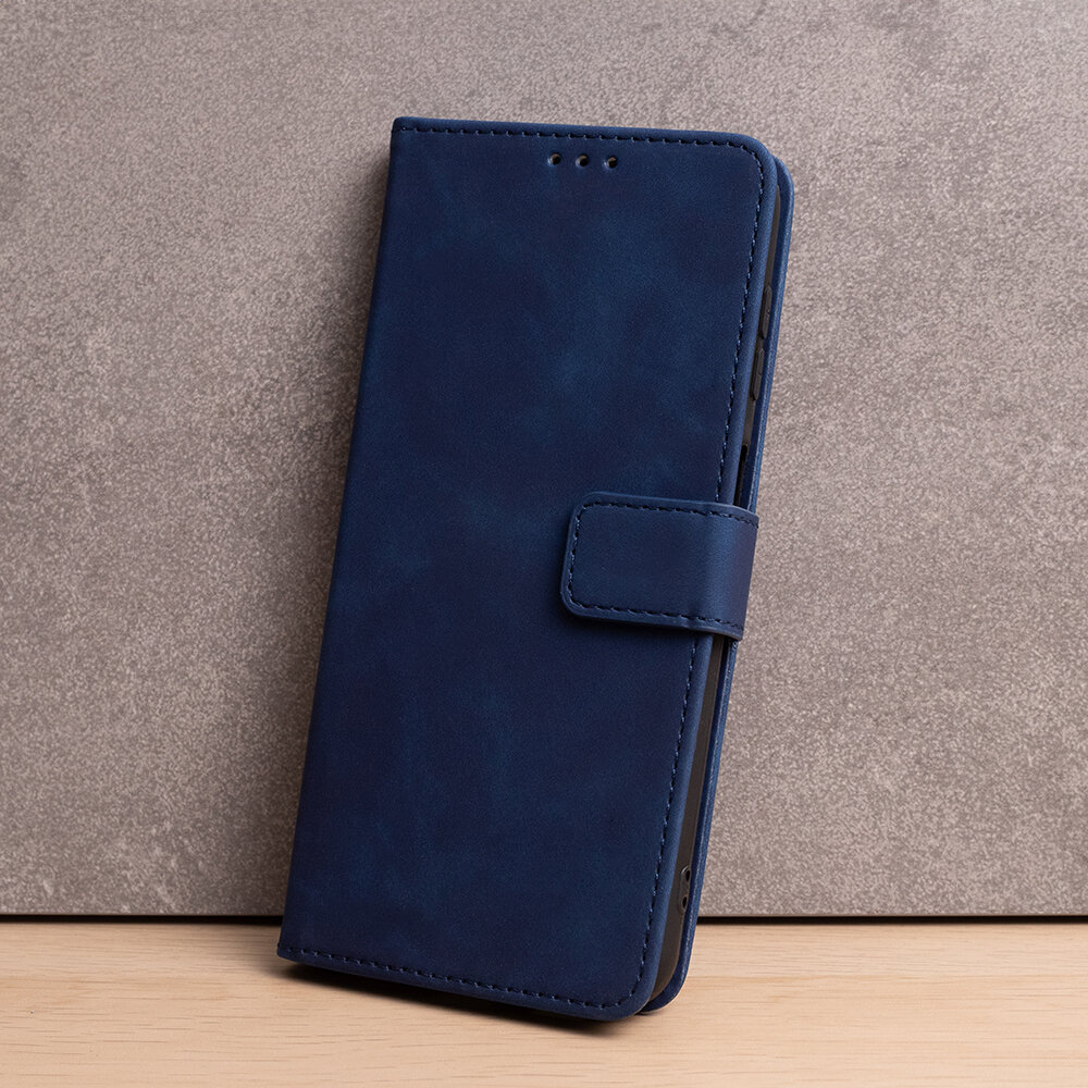 Granatowe etui na telefon z klapką, wykonane z materiału przypominającego zamsz, z widocznym zapięciem na magnes.