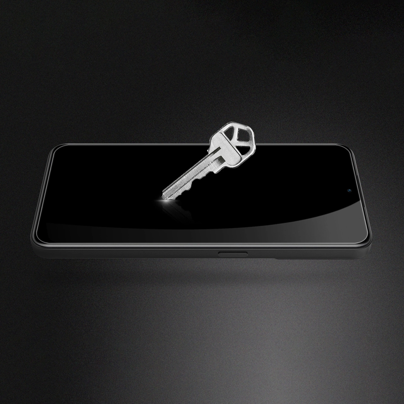 Na ciemnym tle widać smartfon z czarnym ekranem, na którym leży metalowy klucz. Ekran jest gładki i nie ma widocznych zarysowań.