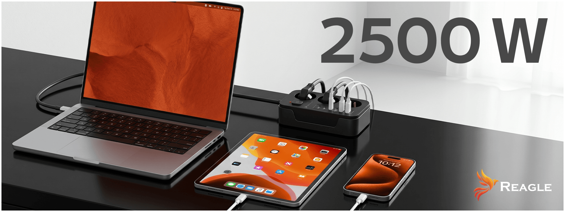 Na biurku znajduje się laptop, tablet i smartfon podłączone do czarnej listwy zasilającej z kilkoma kablami. Widoczny jest napis \'2500 W\' oraz logo \'REAGLE\'.
